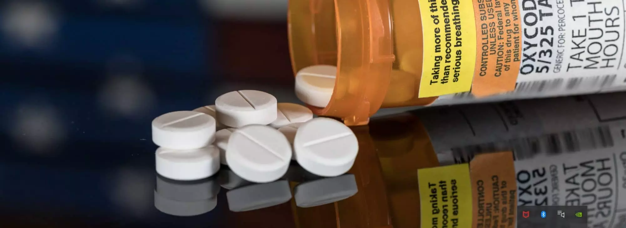 White prescription opioid pills spilling from an orange pill bottle representing opioid addiction and treatment services