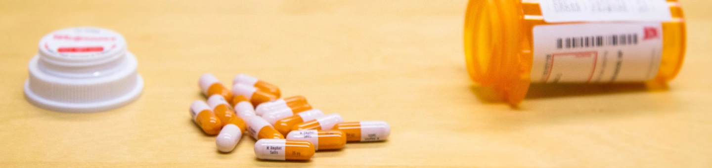 Orange prescription bottle with stimulant capsules spilling out, representing Adderall misuse and addiction