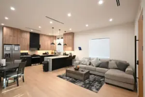 Legacy Healing Center Cleon, Los Angeles – A modern open-concept living room and kitchen with wood cabinetry, stainless steel appliances, island seating, sectional sofa, and soft lighting, creating a comfortable and supportive environment for addiction recovery.