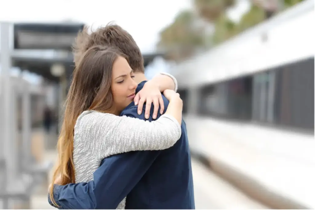 Two people embracing at a train station, sharing an emotional moment before traveling for addiction treatment support.