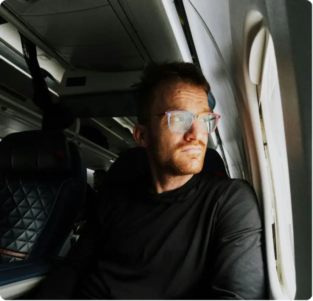 Man sitting in an airplane seat looking out the window, appearing thoughtful during travel for addiction treatment assistance.
